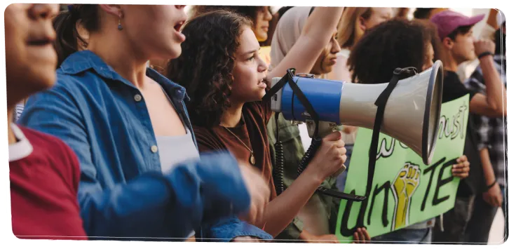 Dans une manifestation regroupant plusieurs personnes, une fille s’exprime dans un haut-parleur.