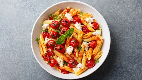 Un bol de penne aux tomates cerises, fromage feta et basilic.
