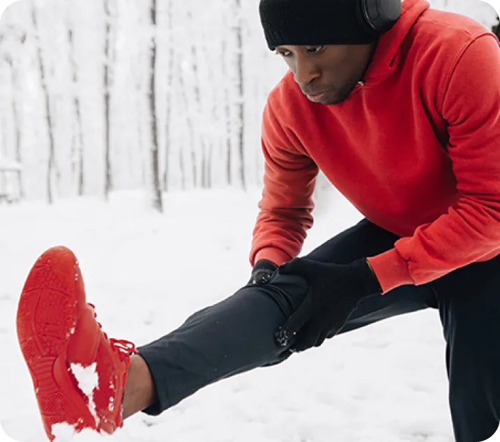 Un jeune homme étirant une jambe dans la forêt en hiver.