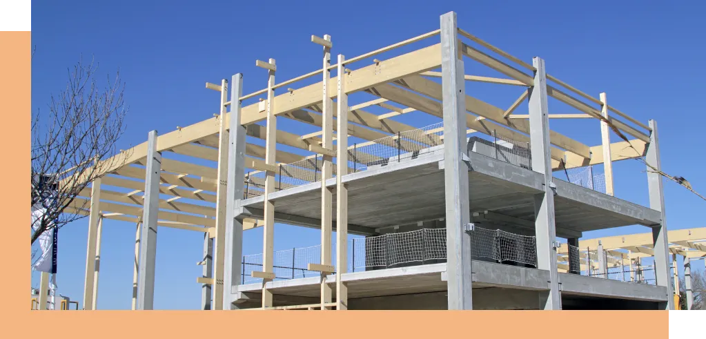 Structure en construction composée d’une ossature en béton et en bois, avec des poutres et des piliers visibles. Le ciel est dégagé en arrière-plan, illustrant un projet en cours de réalisation.