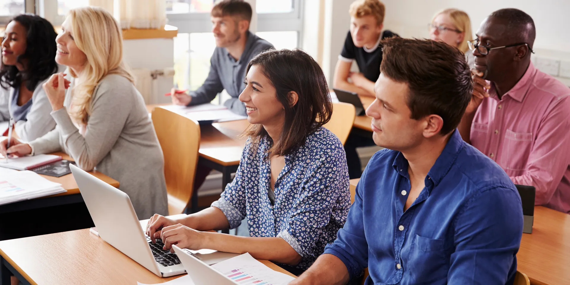 Des adultes de différentes origines culturelles dans une classe, écoutant la personne qui leur enseigne.