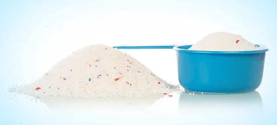 Un tas de granules blanches parsemé de particules de couleur à côté d’une cuillère à mesurer remplie de la même substance.