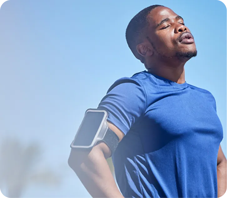 Un jeune homme muni d’un téléphone fixé à son bras ayant les yeux fermés face au soleil.