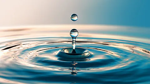 Impact d’une goutte sur l’eau tranquille, dessinant une onde à la surface.