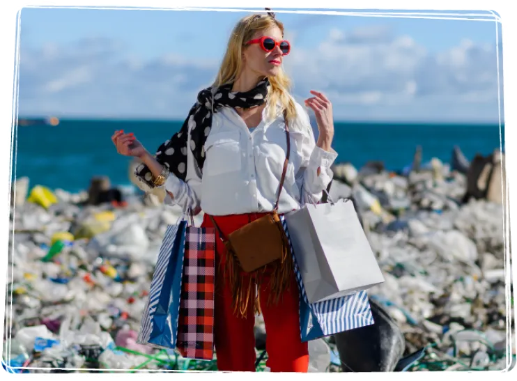 Une jeune femme stylée sur une plage jonchée de déchets, avec plusieurs sacs d’achats accrochés aux bras.